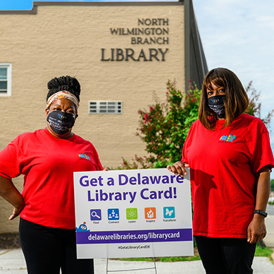 Two members of staff standing in front of a Delaware Library building.