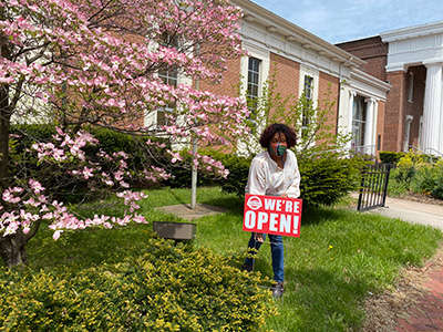 masked woman outside library with a “We’re Open” sign