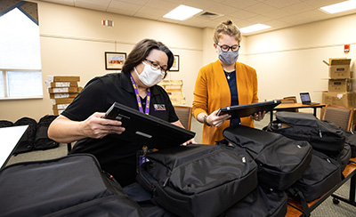 Library staff assemble laptops with bags and headphones.