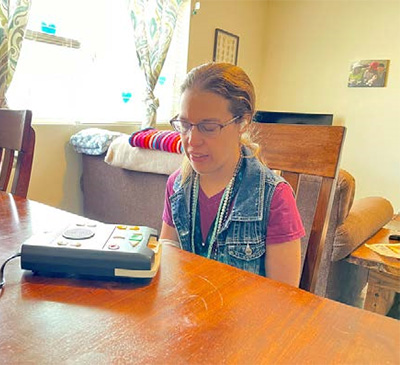 Woman sits at table with audio playback device.