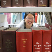 An intern peers out from in between books in the stacks