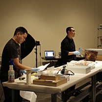 Conservation technician Ryan Ashley (right) and Randall Melton (far left) work on collection objects and explain their methods to a group of visitors during the "Caring for the Past" exhibit.
