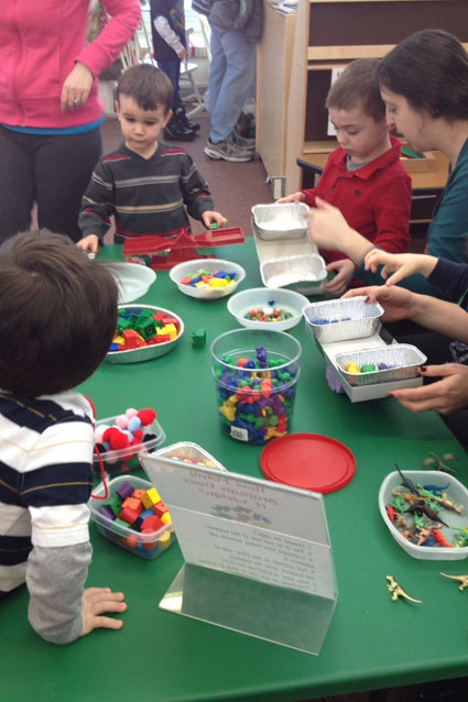 A group of Kingdom of Why participants explore weight with dinosaurs and other toys.