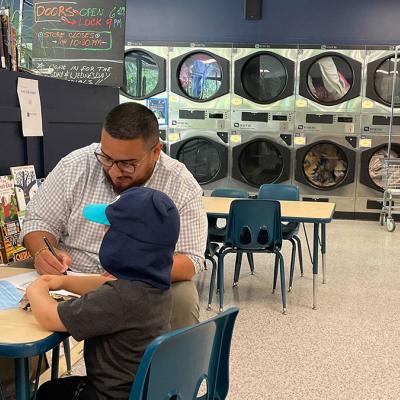 Wash and Learn library participants engage in table activity and a row of coin laundry machines in the background.