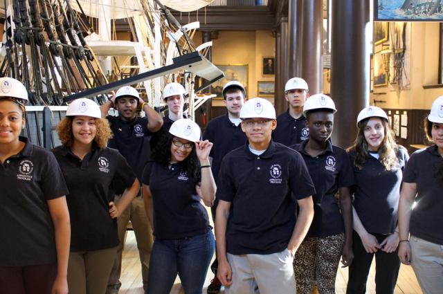 Group of students wearing hard hats, standing in front of museum exhibit.