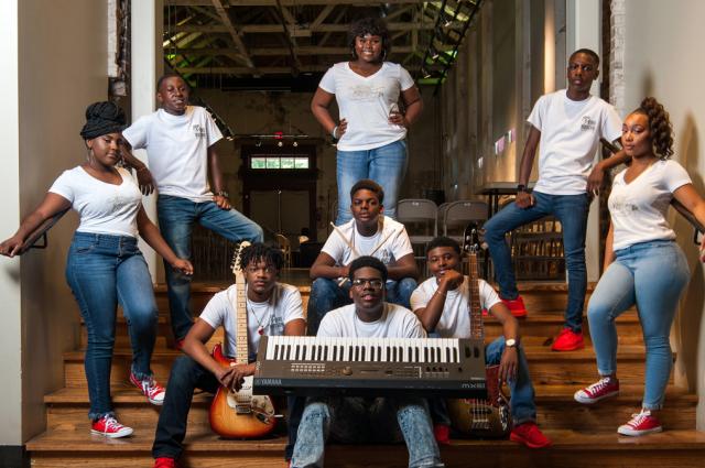 A group of gifted and talented teenagers, dressed in blue jeans and white shirts, pose with musical instruments on stage at the The B.B. King Museum and Delta Interpretive Center.  
