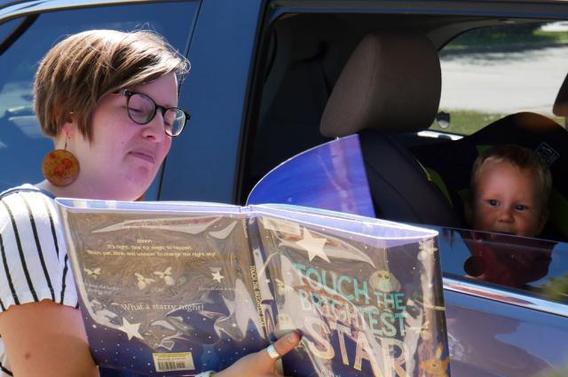 Staff reading book to toddler in a car seat for the Kenosha Public Library Drive Thru Storytime