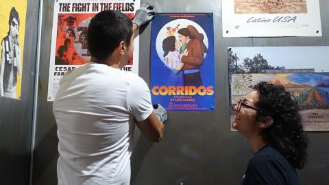 Two young people hang art posters on a wall, National Museum of Mexican Art