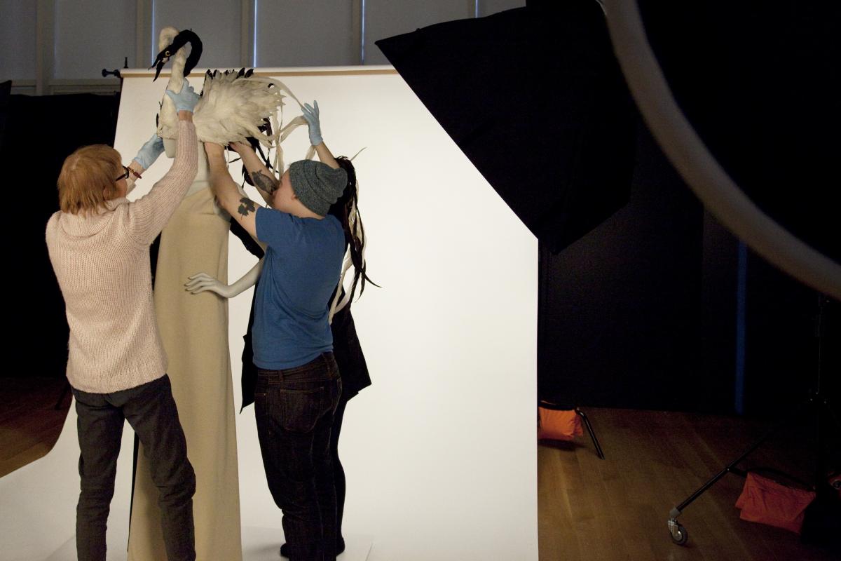 Curator Phyllis Magidson and the Dressing Room project team place a swan headdress designed by William J. Cunningham on a mannequin dressed in an evening gown by James Galanos.  Both were worn by Isabel Eberstadt to Truman Capote’s “Black and White Ball,” 1966. Museum of the City of New York, 67.12 and 77.36.